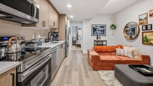 A modern kitchen with stainless steel appliances, a wooden cabinet, and a cozy living area with a sofa and cushions.