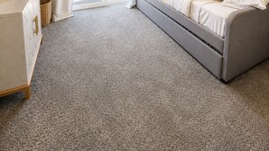 Un dormitorio con cama, mesita de noche, lámpara, planta y puerta corrediza de vidrio que da a un espacio exterior.