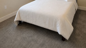 Una habitación de hotel con una cama grande, una mesita de noche, una lámpara y dos ventanas con persianas.