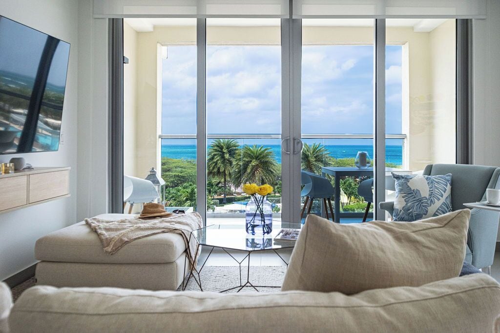A modern living room with a large glass door leading to a balcony with a view of the ocean.