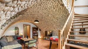 Una habitación acogedora con techo de piedra, escalera de madera, sofá, mesa y televisor.