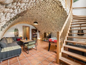 Una habitació acollidora amb sostre de pedra, escala de fusta, sofà, taula i televisor.
