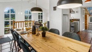 Un comedor amplio con una larga mesa de madera, numerosas sillas, iluminación colgante y vistas al exterior a través de grandes ventanales.