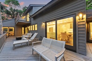Eine Holterrasse mit Sitzgelegenheiten im Freien, eine überdachte Terrasse und Blick in eine moderne Küche.