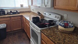 Cucina con pensili e basi in legno, forno a microonde, piano cottura e un ripiano con una macchina da caffè e bottiglie d'acqua.