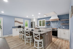 A modern kitchen with a central island, bar stools, a refrigerator, an oven, and a backsplash. - Steps to the Beach on Seabrook! Family Favorite w/ Club Access (Seabrook Island)