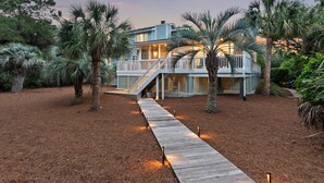 Une maison dotée d’une terrasse en bois donnant sur un porche abrité, le tout entouré de palmiers.
