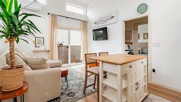 Um espaço de estar moderno com sofá, mesa de jantar, TV e uma janela grande.