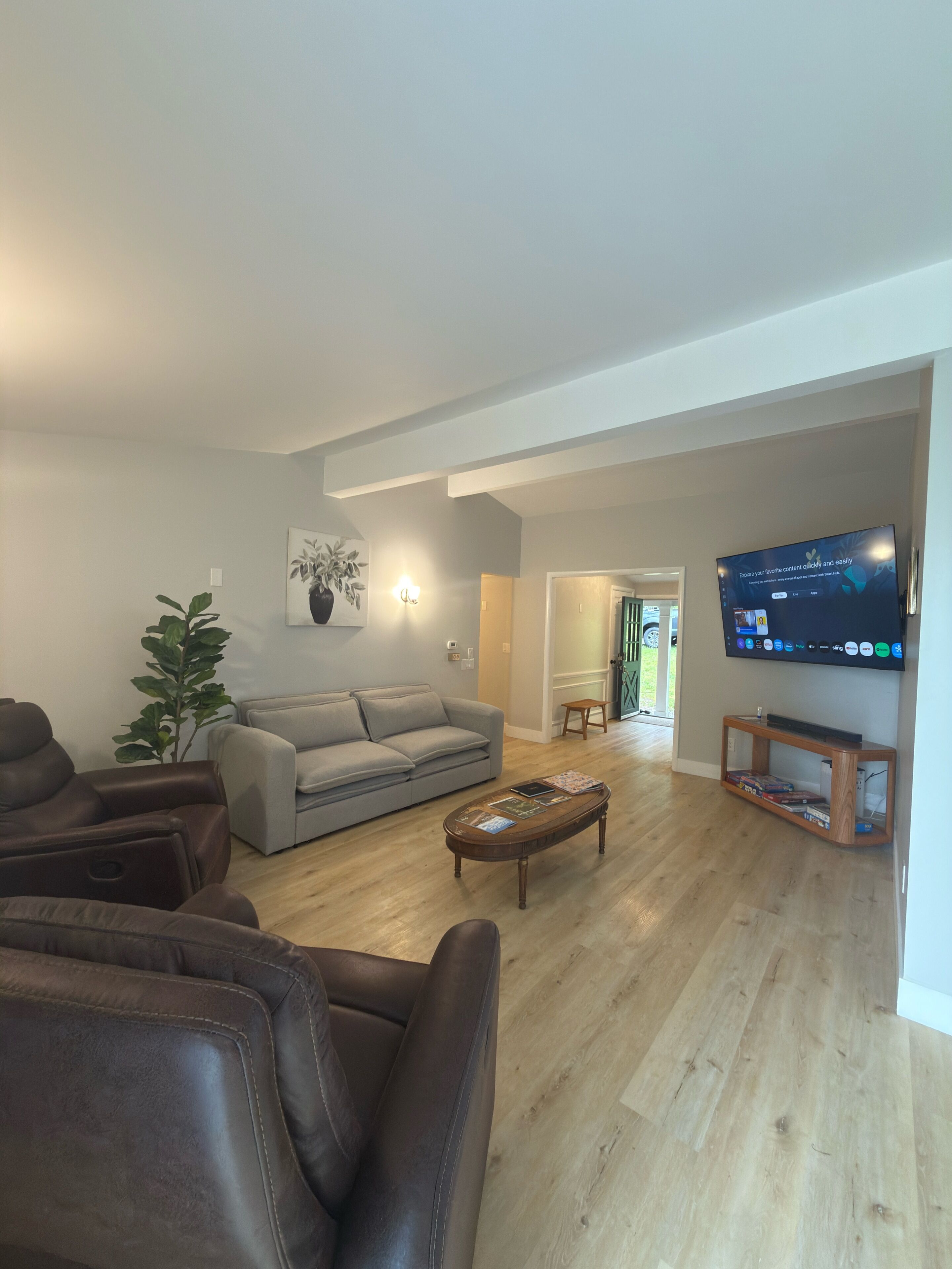 Una sala de estar con un sofá gris, sillones de cuero marrón, una mesa de centro con revistas, un televisor en la pared y piso de madera.