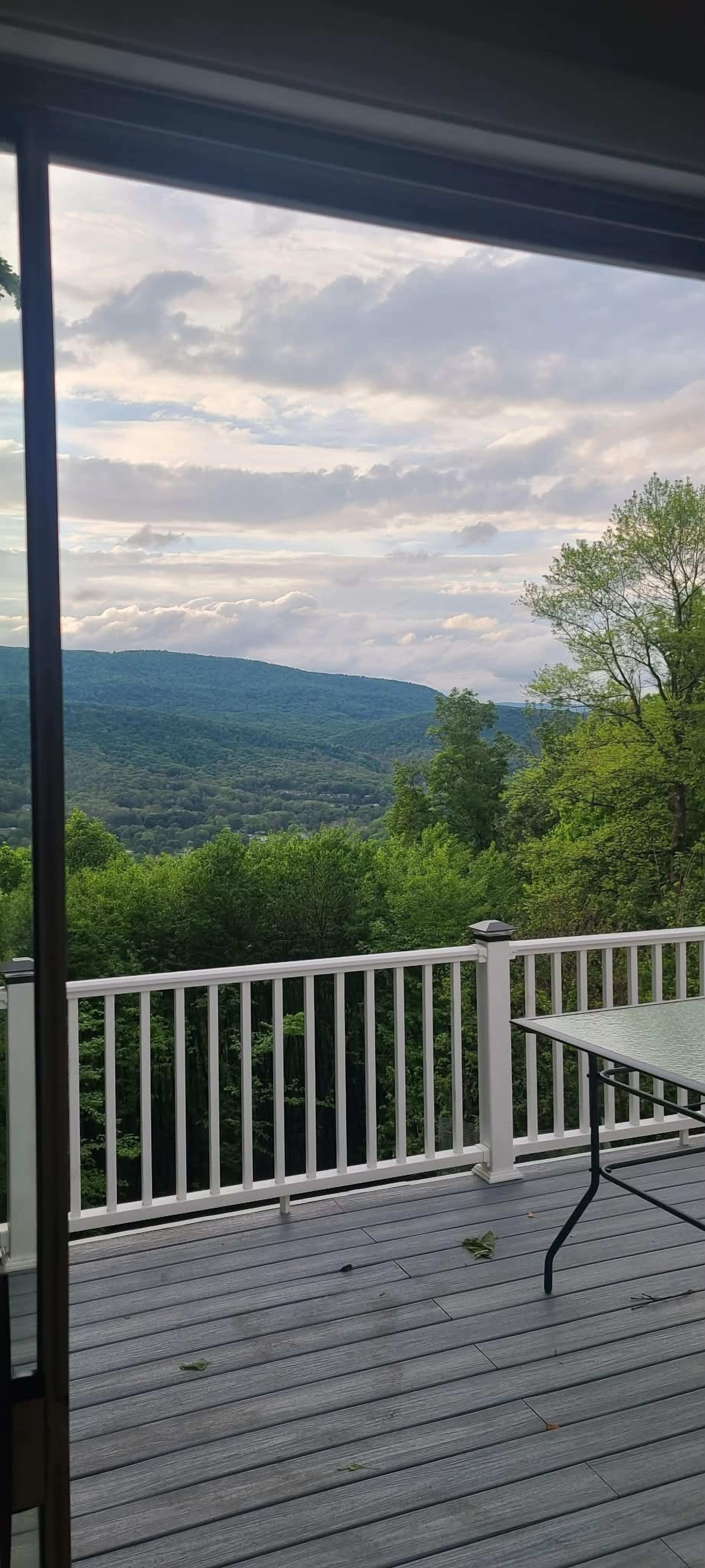 Une terrasse dotée d’une balustrade blanche, d’une table et offrant une vue sur un paysage boisé.