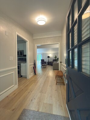 Un couloir avec un plancher en bois, un coin repas avec une table et des chaises, une cuisine équipée et une porte avec une fenêtre.