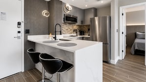 Een moderne keuken met een centraal eiland, twee barkrukken, een roestvrijstalen koelkast en een magnetron.