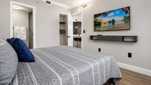Een slaapkamer met een bed, een schilderij, een plank en een badkamer die door een open deur zichtbaar is.