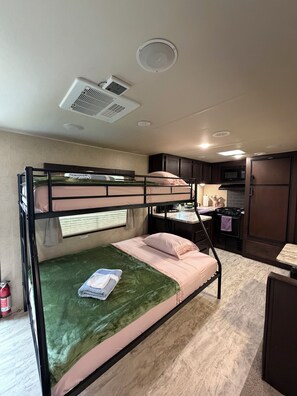 A bunk bed with a green blanket, a kitchenette with a microwave, and a stove.