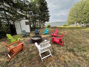 Un patio trasero con sillas Adirondack de varios colores, un brasero y vista a un lago.