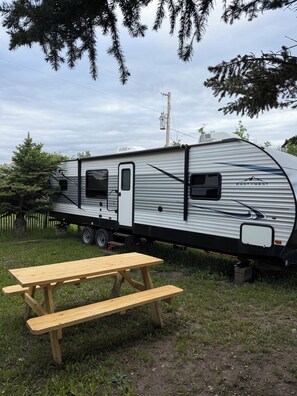 Una caravana estacionada con un porche cubierto, una mesa de picnic y un patio cercado.
