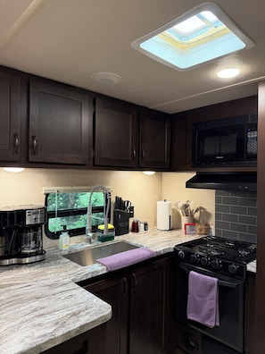 A kitchen with dark wood cabinets, a gas stove, a microwave, a coffee maker, and a window with a view.