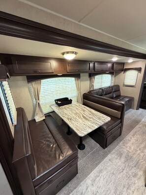 Interior compacto de una caravana con comedor, asientos y compartimentos de almacenamiento.