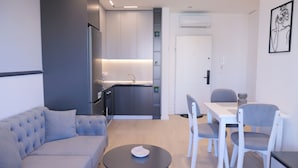 A modern living room with a sofa, a dining table with chairs, a kitchen area, and a door. - Horizont Premium Apart-Hotel (Shkodër)