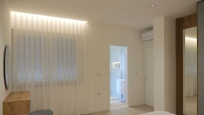 A modern bedroom with a bed, a bedside table, a mirror, and a door leading to a bathroom. - Horizont Premium Apart-Hotel (Shkodër)