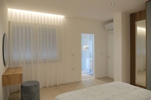 A modern bedroom with a bed, a bedside table, a mirror, and a door leading to a bathroom.