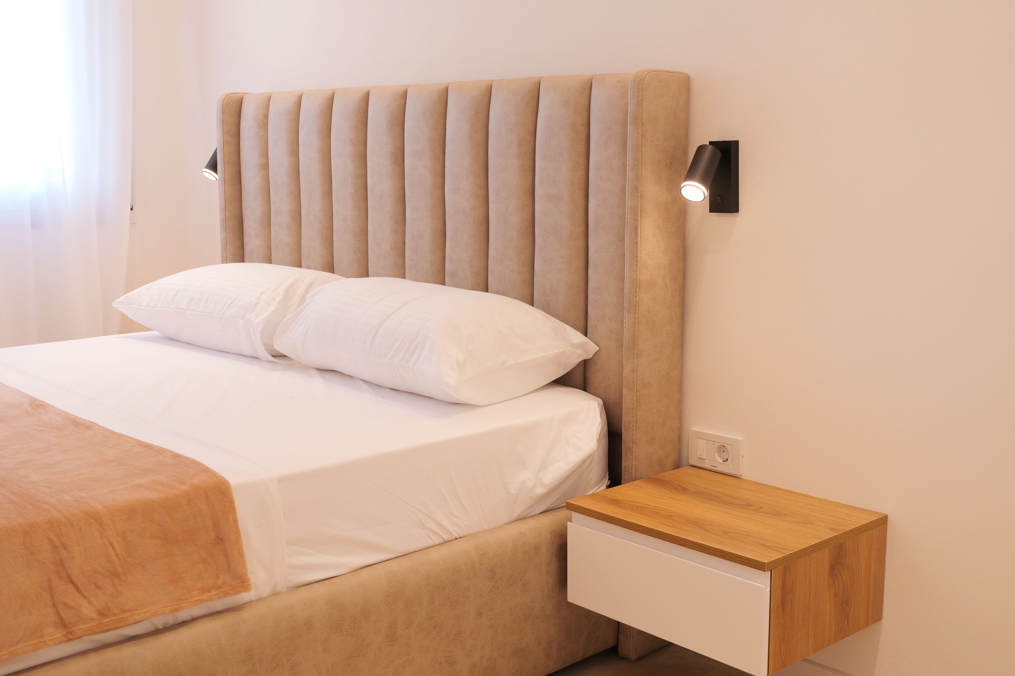 Ein Bett mit Kopfteil, ein Nachttisch mit Schublade und eine Wandleuchte.