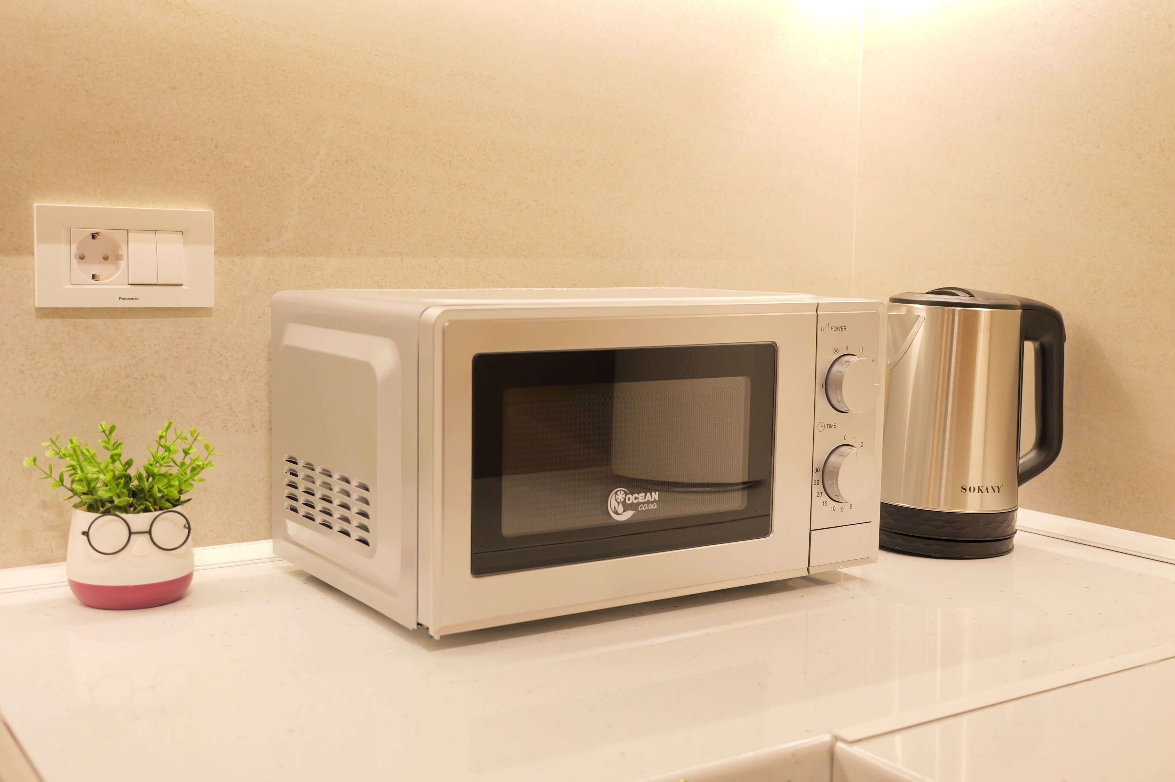 A microwave oven with a transparent door, a coffee maker, and a potted plant with glasses on the counter.