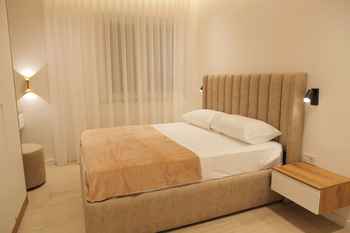 A modern bedroom with a bed, bedside table, and a wall-mounted light.
