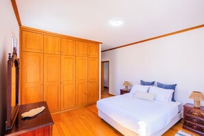 A bedroom with a large wooden wardrobe, a bed with white bedding, two bedside tables with lamps, and a wooden nightstand.