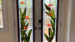 Puertas dobles con vidrieras que representan flores tropicales, suelo de madera y felpudo a rayas.