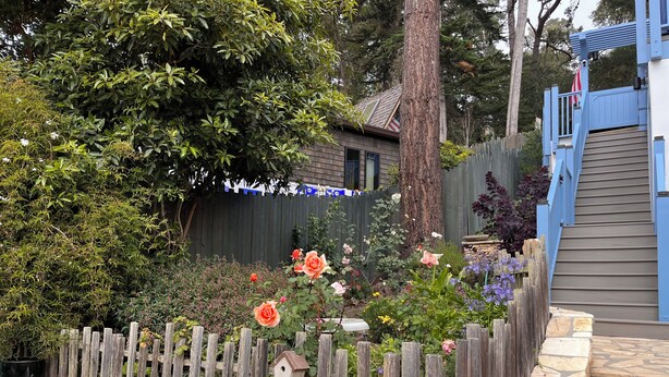 Un jardín con cerda de madera, un comedero para pájaros y un muro de piedra.