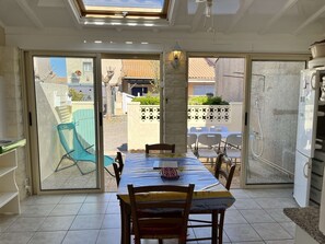 Ein Essbereich mit Tisch, Stühlen, einem Deckenventilator und Blick durch große Glasfenster nach draußen.