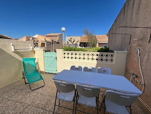 Eine Terrasse im Freien mit Tisch und Stühlen, einem türkisblauen Tor und einer Wand mit Muster.