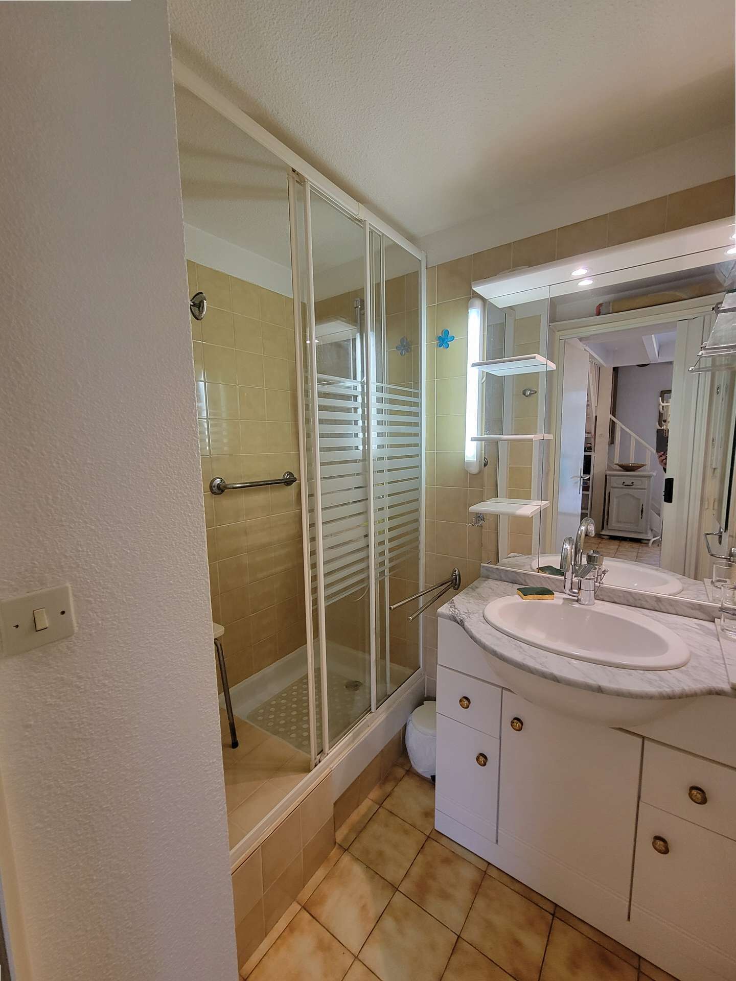 A bathroom with a glass-enclosed shower, a white sink with a mirror, and beige tiles.