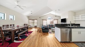 A spacious living area with a dining table, chairs, a sofa, and a kitchen area with a dishwasher and a TV. - NRG Stadium Steps Away- Perfect World Cup Stay w/ Parking and Security Gates (Houston)