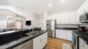 A modern kitchen with a black countertop, stainless steel appliances, white cabinets, and a wooden floor. - NRG Stadium Steps Away- Perfect World Cup Stay w/ Parking and Security Gates (Houston)