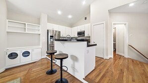 A modern kitchen with white cabinets, a central island, and two stools. - NRG Stadium Steps Away- Perfect World Cup Stay w/ Parking and Security Gates (Houston)