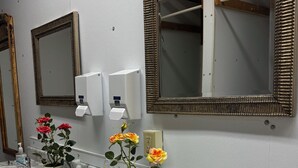 Un baño con tres lavamanos, dos dispensadores de jabón para manos y dos espejos con marcos decorativos.