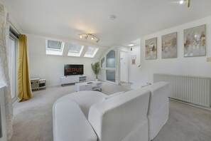 A modern living room with a TV, white furniture, and artwork on the walls. - Cove Lodge - Grampian Lettings (Aberdeen)