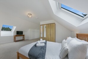 A bedroom with a skylight, a bed with white bedding, a wooden wardrobe, and a television on a stand. - Cove Lodge - Grampian Lettings (Aberdeen)