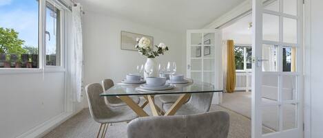 A dining area with a glass table, grey chairs, and a vase of flowers.