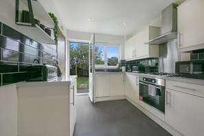 A modern kitchen with white cabinets, a built-in oven, a microwave, and a gas stove. - Cove Lodge - Grampian Lettings (Aberdeen)