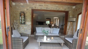 An open-plan living area with wicker furniture, a stone wall, and a view into the kitchen. - Your Provençal Escape among Olive Trees, with a Private Pool (CALLAS)