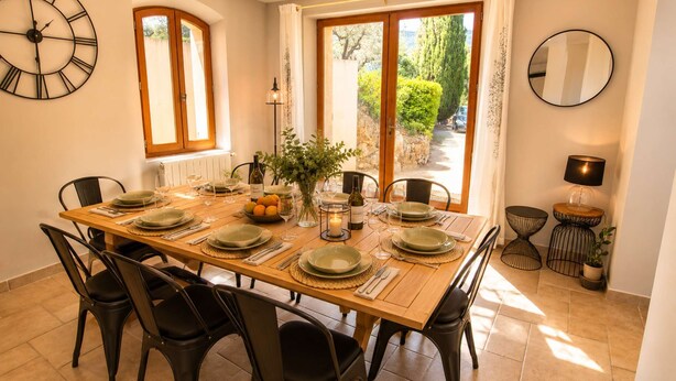 A dining room with a wooden table set for six, black chairs, a large wall clock, and a view through the glass doors. - Your Provençal Escape among Olive Trees, with a Private Pool (CALLAS)