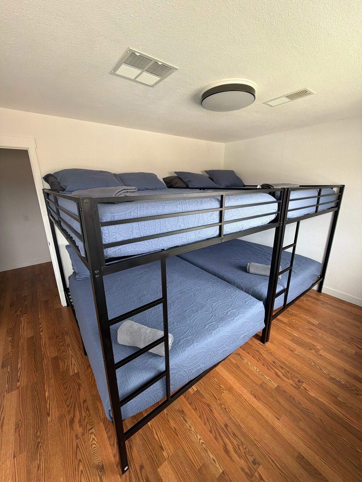 A bunk bed with a headboard, a ceiling vent, and a wooden floor.