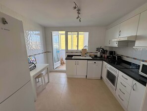 A kitchen with white cabinets, a black countertop, a dishwasher, an oven, and a window with a view of the outside. - Beachnear modern apartment with community pool (Dénia)