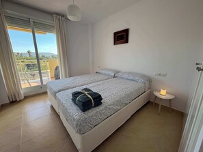A bedroom with two beds, a small bedside table with a lamp, a window with curtains, and a framed certificate on the wall. - Beachnear modern apartment with community pool (Dénia)