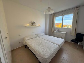 A bedroom with two beds, a window with a view, a chair, and a shelf with decorative items. - Beachnear modern apartment with community pool (Dénia)