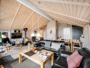 Ein großzügiger Wohnbereich mit hoher Decke, einem Kamin, Ledersofas, einem Esstisch und einer im Hintergrund sichtbaren Küche.