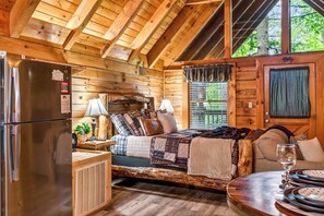 Interior de una cabaña de madera con cama, mesa de comedor y refrigerador.